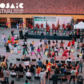 Aerial shot of a group of people in front of an outdoor stage dancing under colored flags