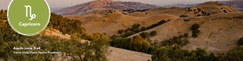 Aquila Loop Trail with brown mountains and a sunset in the background. Capricorn symbol in the left corner.