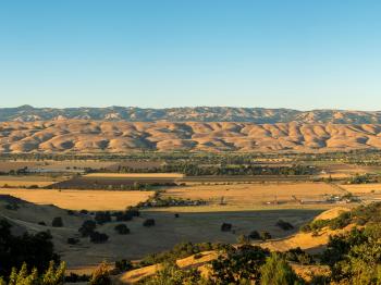 Looking across Coyote Valley, covered in golden fields and farmlands, towards rolling golden hills in the distance all under a blue sky