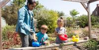 Two children with an adult work together to water a garden