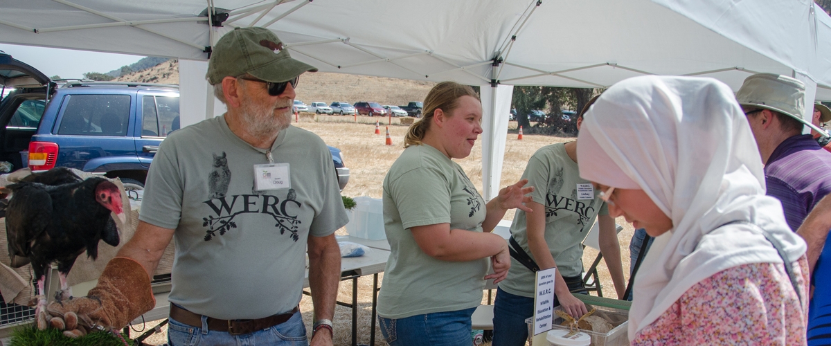 Three people in Wildlife Education and Rehabilitation Center t-shirts with live birds talking to visitors at a booth