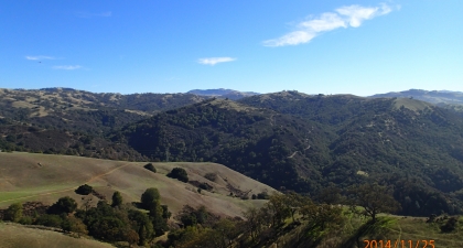 Green and brown hillsides covered in trees under blue sky