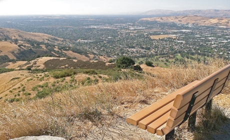 Bench at top of hill overlooking brown summer hillsides and city of San Jose far below