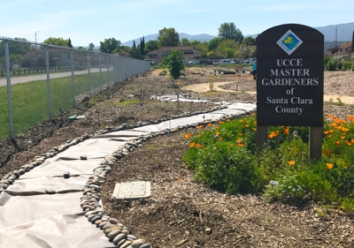 Path leading around garden and wooden sign with UC Master Gardeners of Santa Clara County name and logo