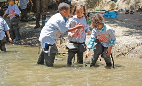 Three children wearing Boys and Girls Club t-shirts playing with small fish nets in creek