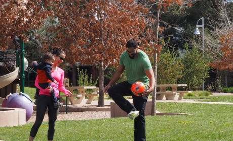 Parents with small child smiling and playing with soccer ball at Stojanovich Family Park