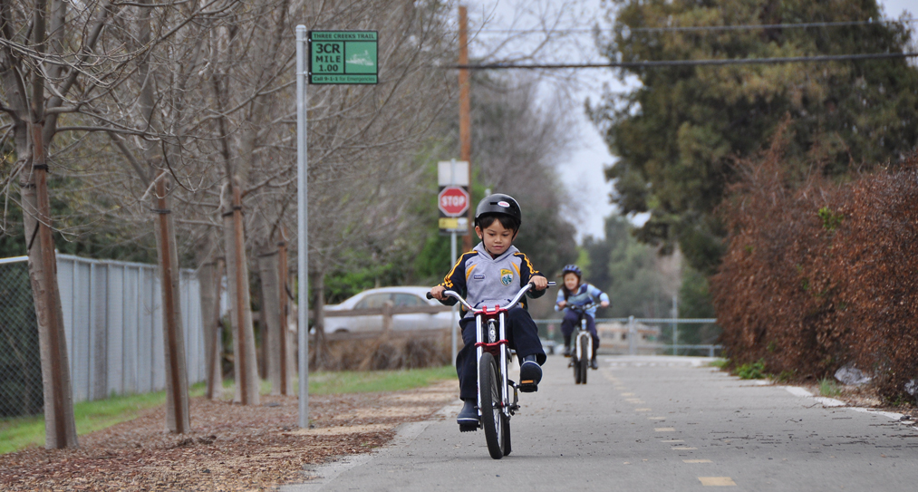 Young boy riding bike on paved trail with older girl on bike behind him