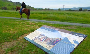 Interpretive panel on the De Anza Expedition in foreground, man on horseback on trail in background