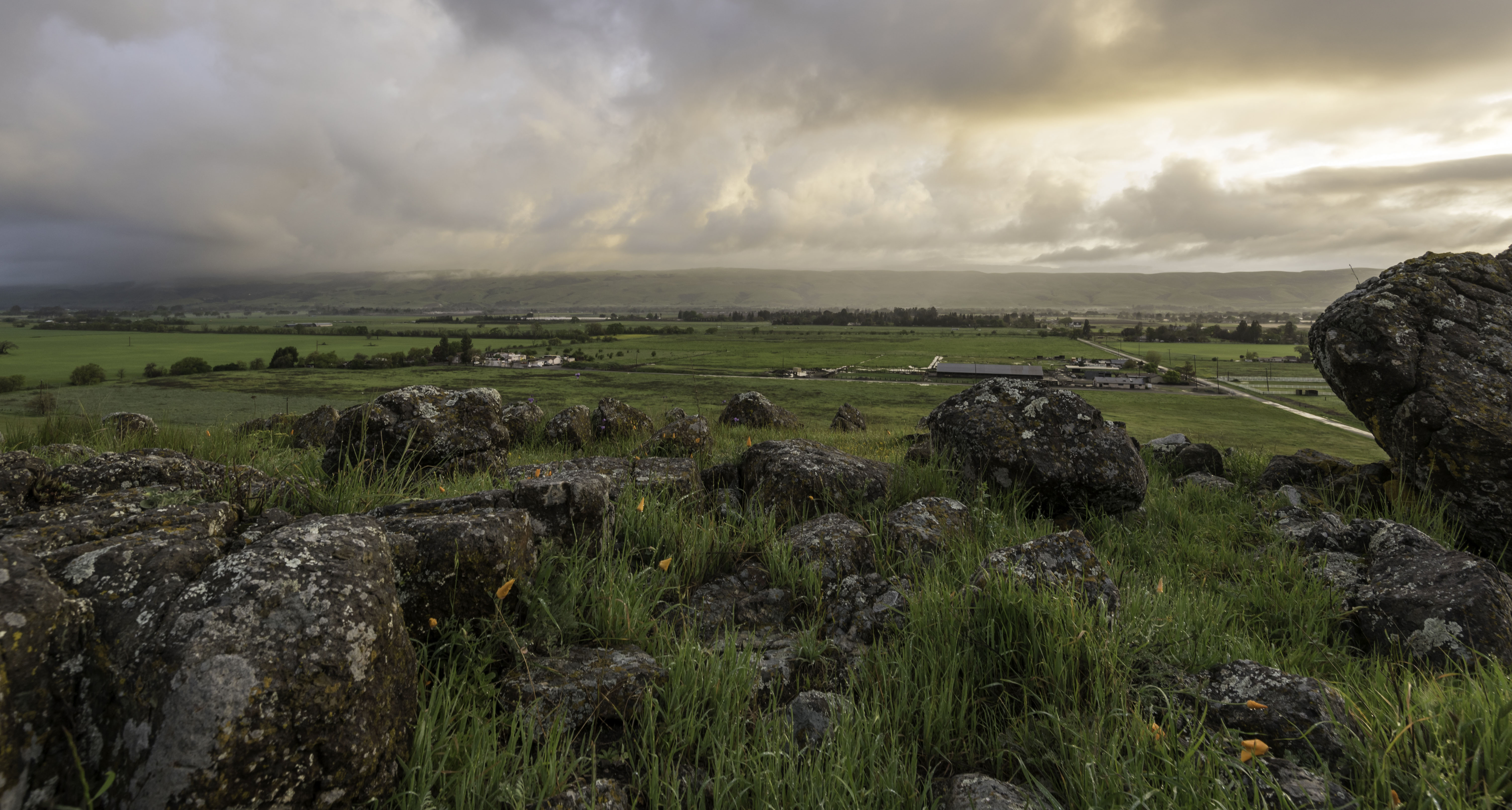 Rocks and green grass overlooking expansive valley with clouds in distance
