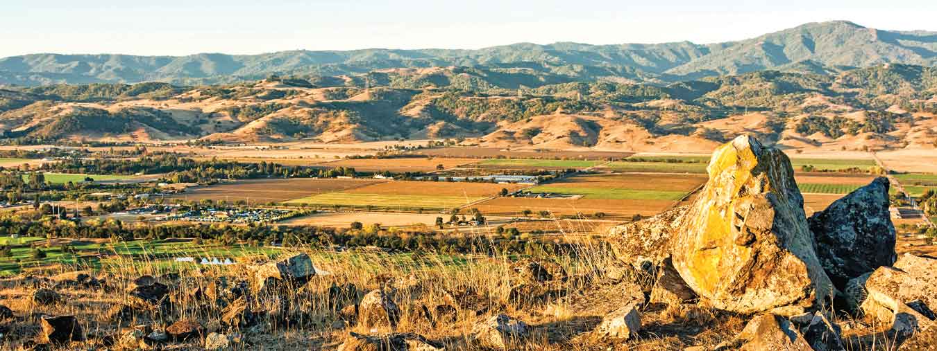 Lichen-covered rocks on ridge overlooking Coyote Valley with agricultural fields and the mountains in the distance